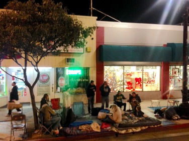 It is getting late and cold but people are settling in to spend the night on the sidewalk.